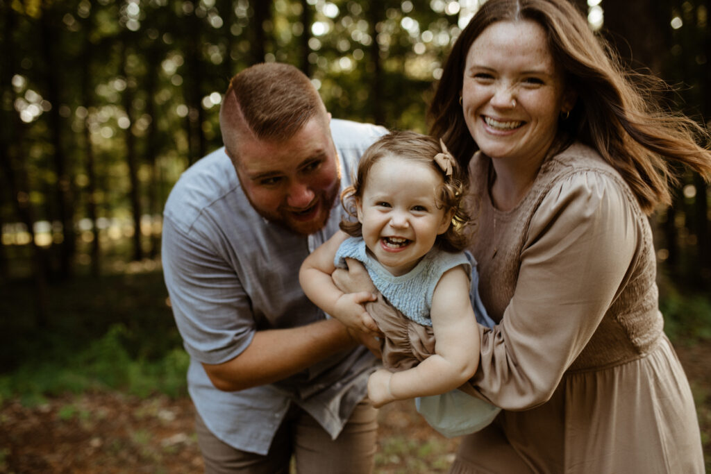 mom and dad run towards the photographer while carrying daughter full of giggles